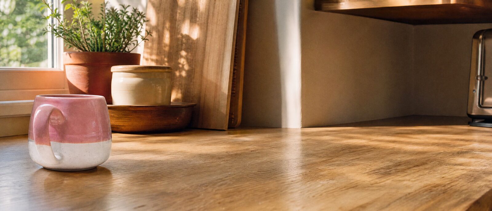 La taza rosa y blanca sobre una encimera de madera con luz de mañana