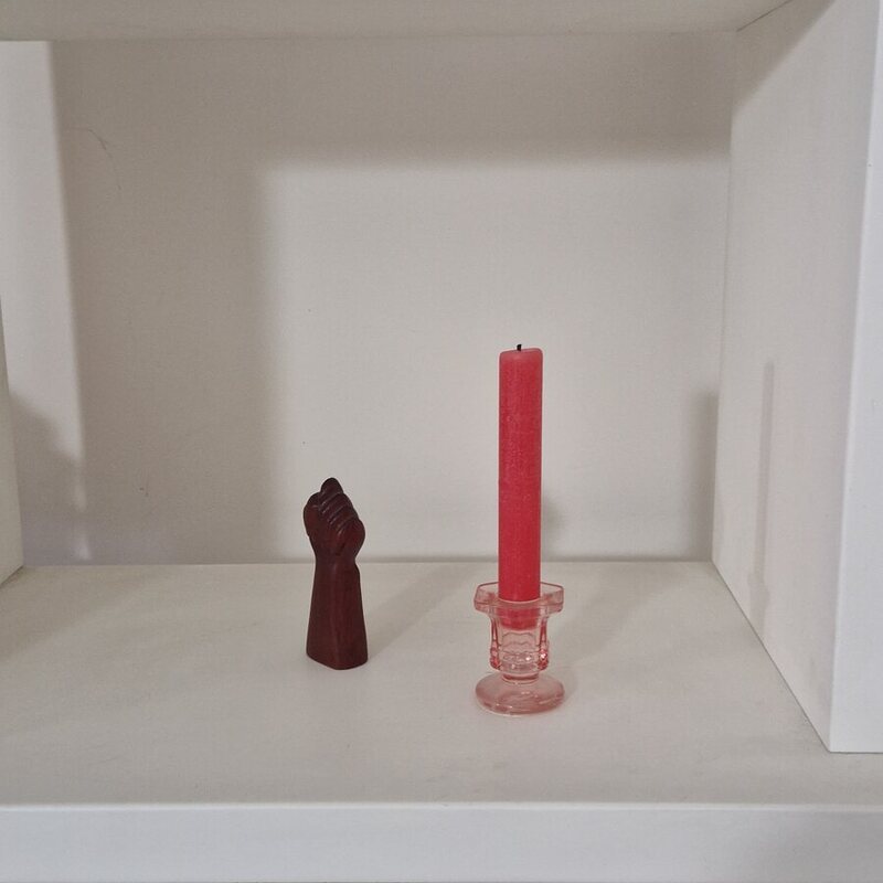 Foto real hecha con el móvil: la vela roja en su candelabro, en una estantería blanca junto a una figura de madera